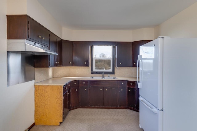 kitchen with freestanding refrigerator, a sink, decorative backsplash, light countertops, and dark brown cabinetry