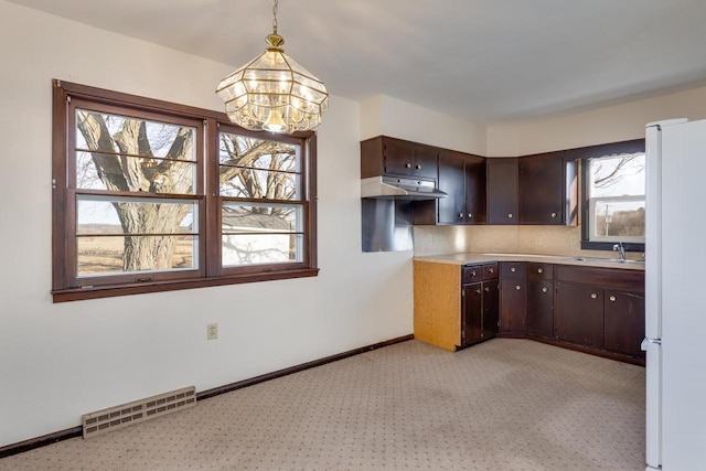 kitchen with visible vents, under cabinet range hood, freestanding refrigerator, a notable chandelier, and a sink