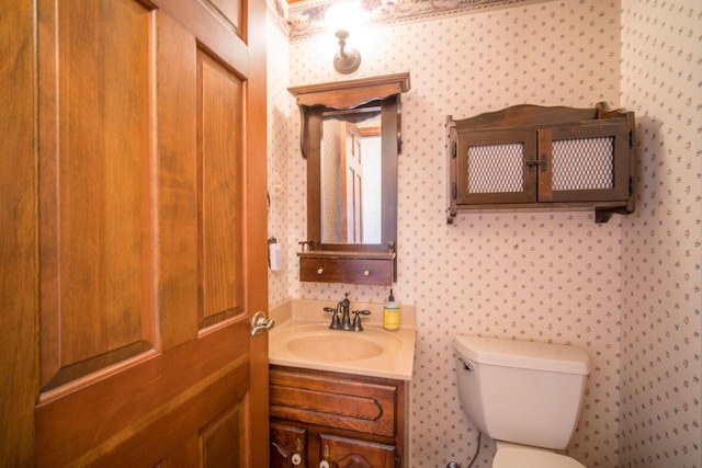 bathroom featuring toilet, vanity, and wallpapered walls