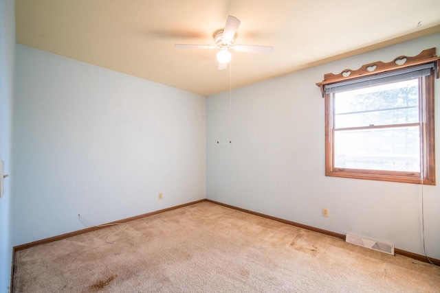 empty room featuring a ceiling fan, light colored carpet, visible vents, and baseboards