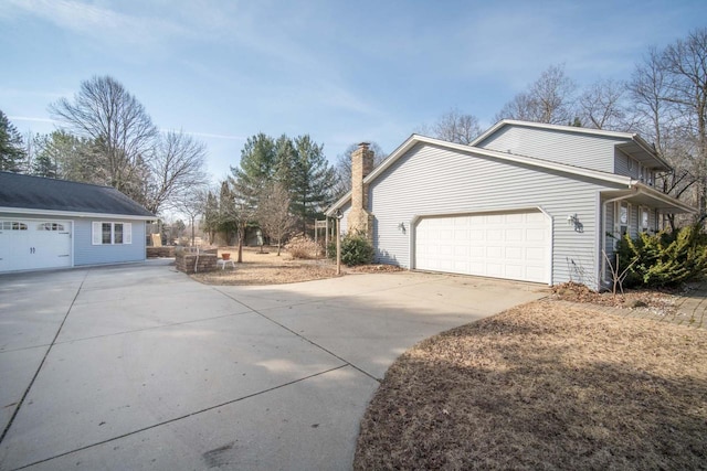 view of property exterior featuring an attached garage, a chimney, and driveway