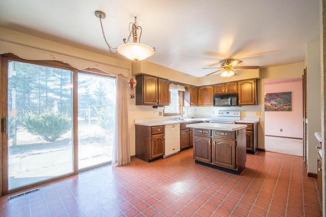 kitchen with a kitchen island, baseboards, ceiling fan, light countertops, and white appliances