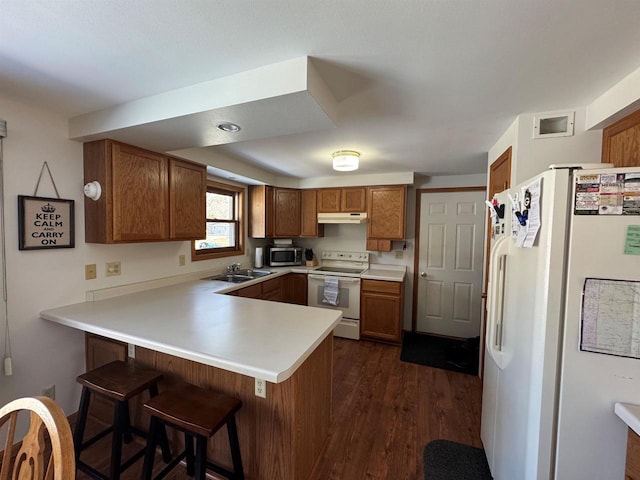 kitchen featuring brown cabinets, under cabinet range hood, a sink, white appliances, and a peninsula