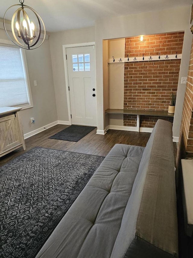 interior space featuring dark wood-style floors, baseboards, a chandelier, and brick wall