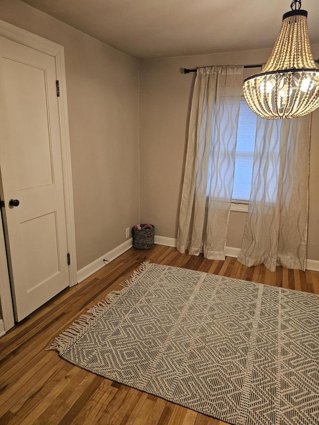 unfurnished room with baseboards, a notable chandelier, and wood finished floors