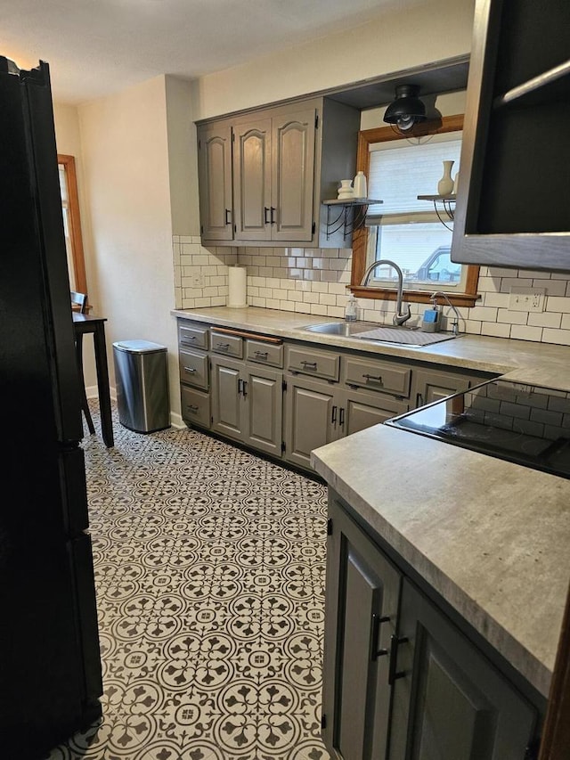 kitchen featuring tile patterned flooring, tasteful backsplash, gray cabinets, freestanding refrigerator, and a sink