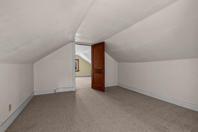 additional living space with carpet flooring, a textured ceiling, baseboards, and vaulted ceiling