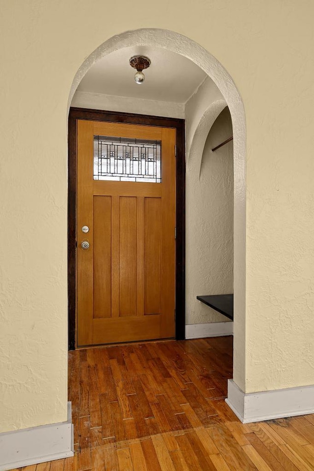 doorway to outside featuring hardwood / wood-style floors, a textured wall, arched walkways, and baseboards