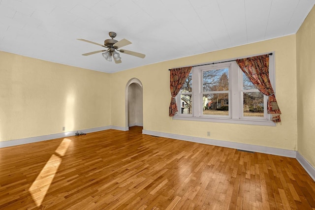 empty room featuring arched walkways, light wood-style flooring, baseboards, and ceiling fan