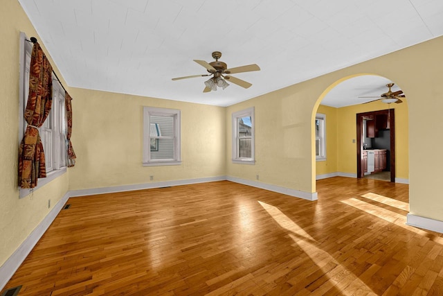 empty room with visible vents, baseboards, light wood finished floors, arched walkways, and ceiling fan