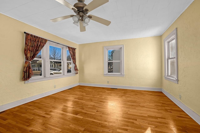 empty room featuring a textured wall, baseboards, light wood finished floors, and ceiling fan