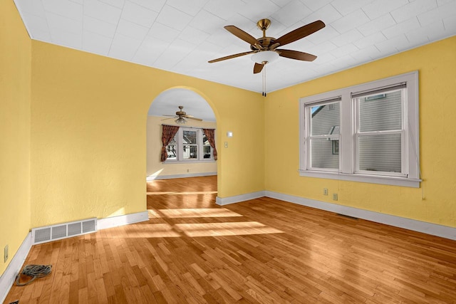 unfurnished room with wood finished floors, a ceiling fan, visible vents, and baseboards