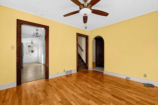 empty room featuring stairway, wood finished floors, visible vents, arched walkways, and ceiling fan