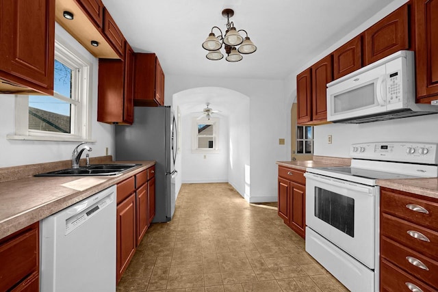 kitchen with ceiling fan with notable chandelier, a sink, white appliances, light countertops, and baseboards