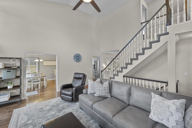 living room featuring baseboards, stairway, ceiling fan with notable chandelier, wood finished floors, and high vaulted ceiling