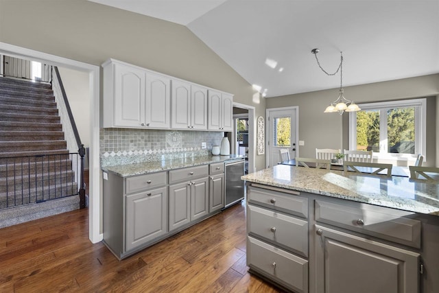 kitchen with lofted ceiling, gray cabinets, decorative backsplash, stainless steel dishwasher, and a chandelier