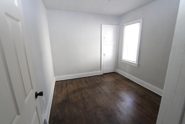 empty room featuring visible vents, baseboards, and dark wood finished floors