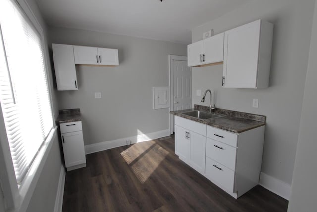 kitchen featuring dark countertops, baseboards, dark wood-style flooring, and a sink