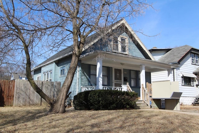 view of front facade featuring covered porch, a shingled roof, and fence