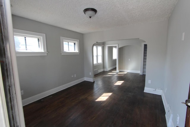 unfurnished room featuring a healthy amount of sunlight, arched walkways, dark wood-style flooring, and baseboards