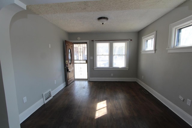 foyer entrance with visible vents, a textured ceiling, baseboards, and dark wood-style flooring