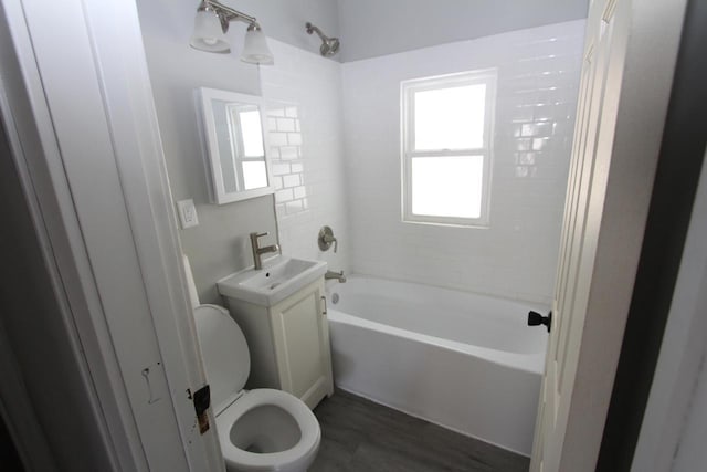 bathroom featuring wood finished floors, washtub / shower combination, toilet, and a sink