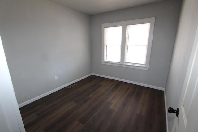 unfurnished room with dark wood finished floors, visible vents, and baseboards