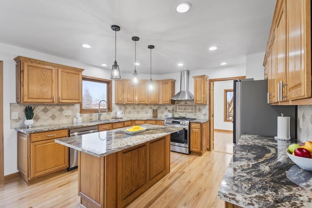 kitchen featuring a sink, stainless steel appliances, light wood-style floors, wall chimney exhaust hood, and light stone countertops