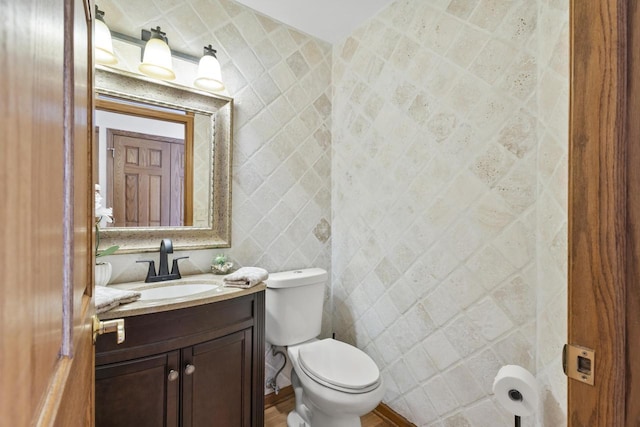 half bath with toilet, tile walls, and vanity