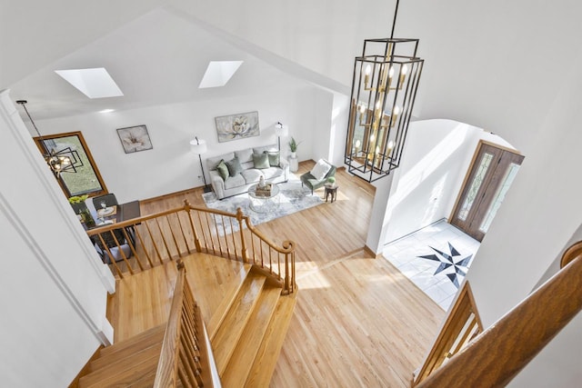 stairs featuring arched walkways, a notable chandelier, lofted ceiling with skylight, and wood finished floors