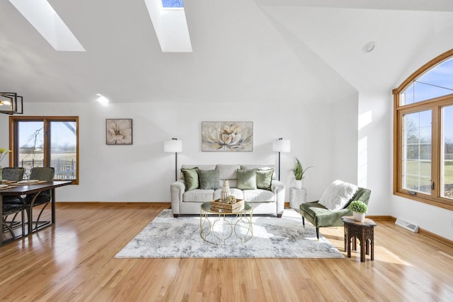 living room with visible vents, plenty of natural light, wood finished floors, and vaulted ceiling with skylight