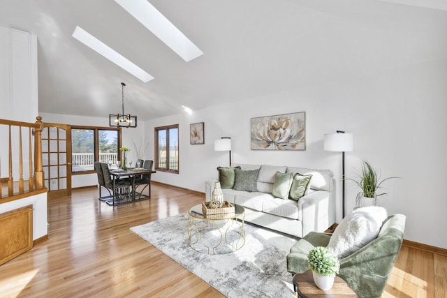 living room with lofted ceiling with skylight, light wood finished floors, baseboards, and an inviting chandelier