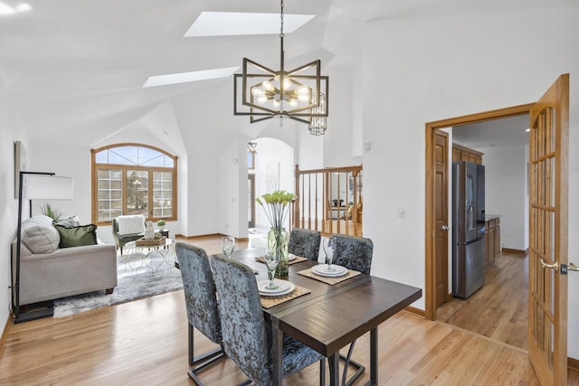 dining area featuring a skylight, light wood-style floors, a chandelier, and high vaulted ceiling