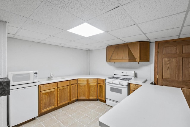 kitchen with white appliances, brown cabinetry, a sink, light countertops, and custom range hood