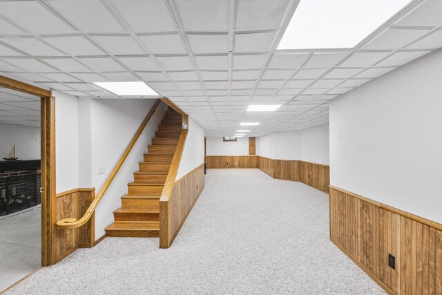 finished basement featuring stairs, a wainscoted wall, wood walls, and carpet flooring