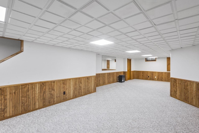 finished basement featuring wooden walls, wainscoting, carpet flooring, and a paneled ceiling