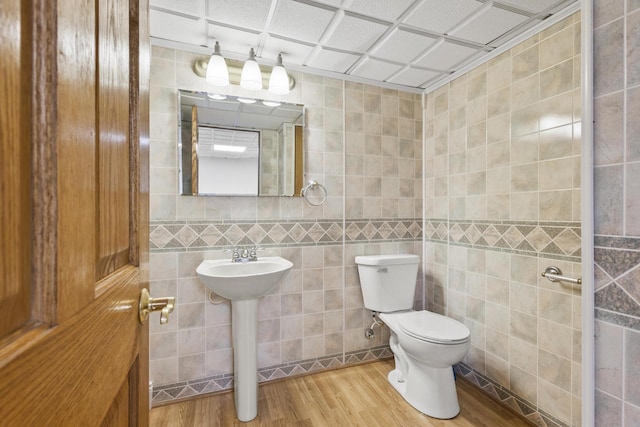 bathroom with tile walls, toilet, wood finished floors, and a sink