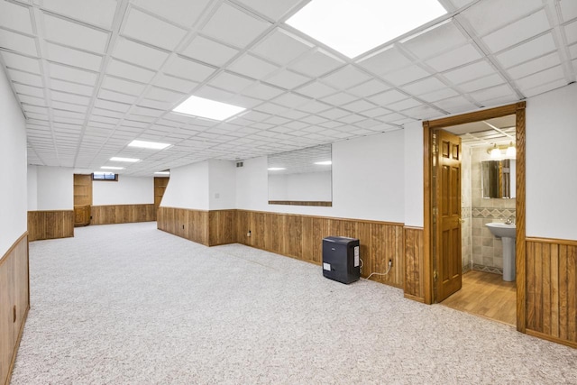 finished below grade area featuring a drop ceiling, a wainscoted wall, carpet, and wood walls