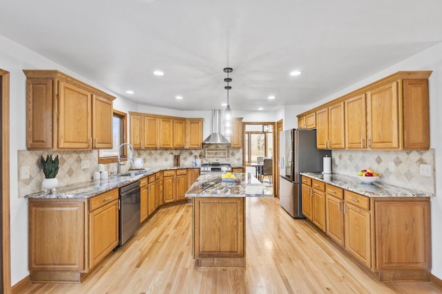 kitchen with a kitchen island, a sink, stainless steel appliances, light wood-style floors, and wall chimney exhaust hood