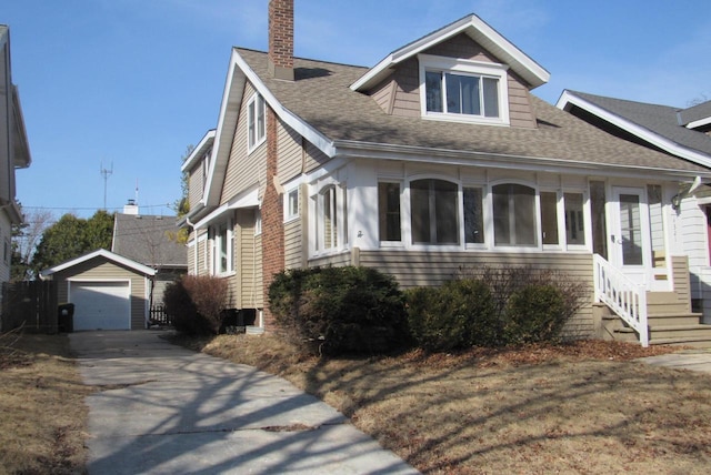 view of front facade featuring a shingled roof, entry steps, concrete driveway, a chimney, and an outbuilding