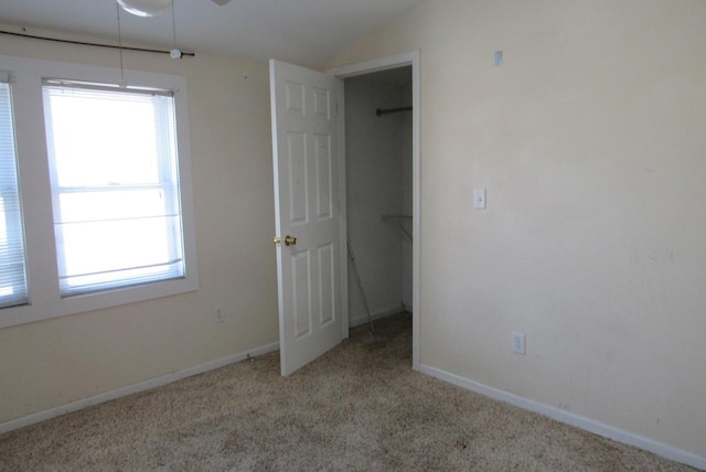 unfurnished bedroom featuring a walk in closet, baseboards, lofted ceiling, carpet floors, and a closet