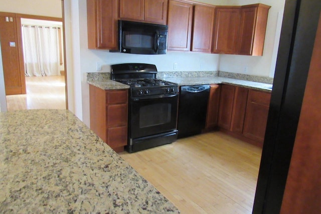 kitchen featuring light wood finished floors, brown cabinets, black appliances, and light stone counters