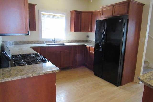 kitchen featuring gas range, light stone counters, light wood-style floors, black refrigerator with ice dispenser, and a sink