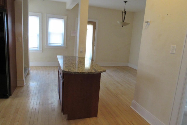 kitchen featuring baseboards, light wood-style flooring, light stone countertops, and freestanding refrigerator