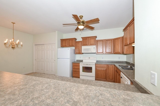 kitchen featuring ceiling fan with notable chandelier, brown cabinets, hanging light fixtures, white appliances, and a sink