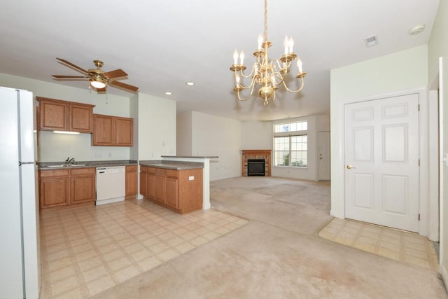 kitchen with a sink, white appliances, a peninsula, light floors, and a brick fireplace