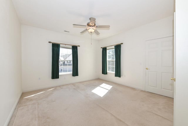 carpeted spare room featuring baseboards, plenty of natural light, a ceiling fan, and visible vents