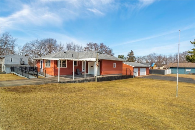 rear view of property featuring an outdoor structure, a lawn, fence, and aphalt driveway