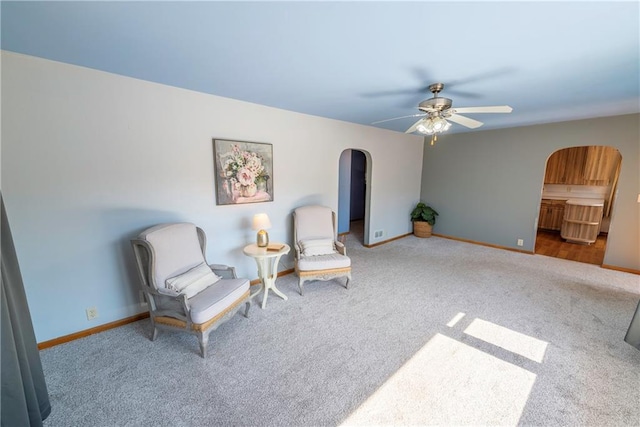 living area with arched walkways, baseboards, ceiling fan, and carpet floors