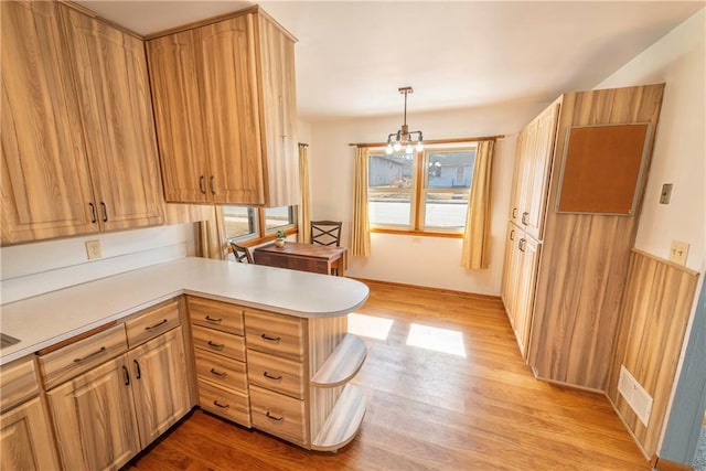 kitchen with light countertops, a peninsula, light wood-type flooring, and pendant lighting